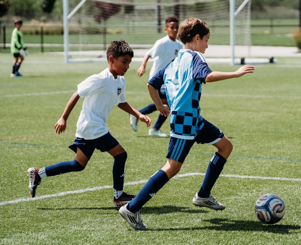 An SBV U11 boys player in the sky and navy checkered kit dribbling past a defender